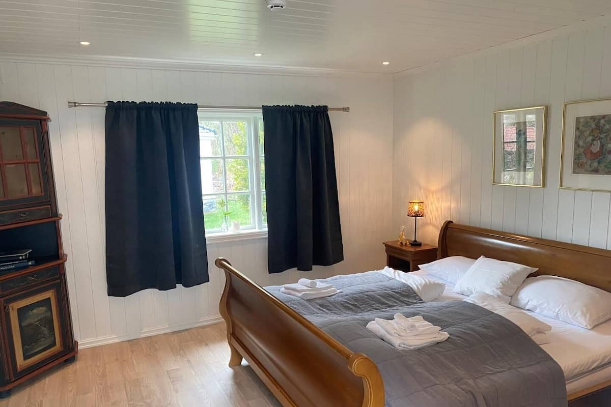 Ein Schlafzimmer mit einem hölzernen Bett, einem Nachttisch mit Lampe, einem Fenster mit Vorhängen und einem Schrank.