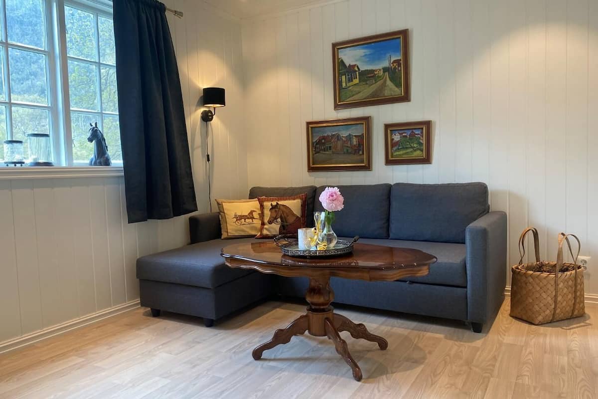 Ein Wohnzimmer mit grauem Sofa, einem Holztisch mit Vase und Tablett, einer Lampe und gerahmten Bildern an der Wand.