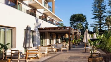 En hotelterrasse med udendørs møbler, et overdækket område og udsigt til bygningens facade.