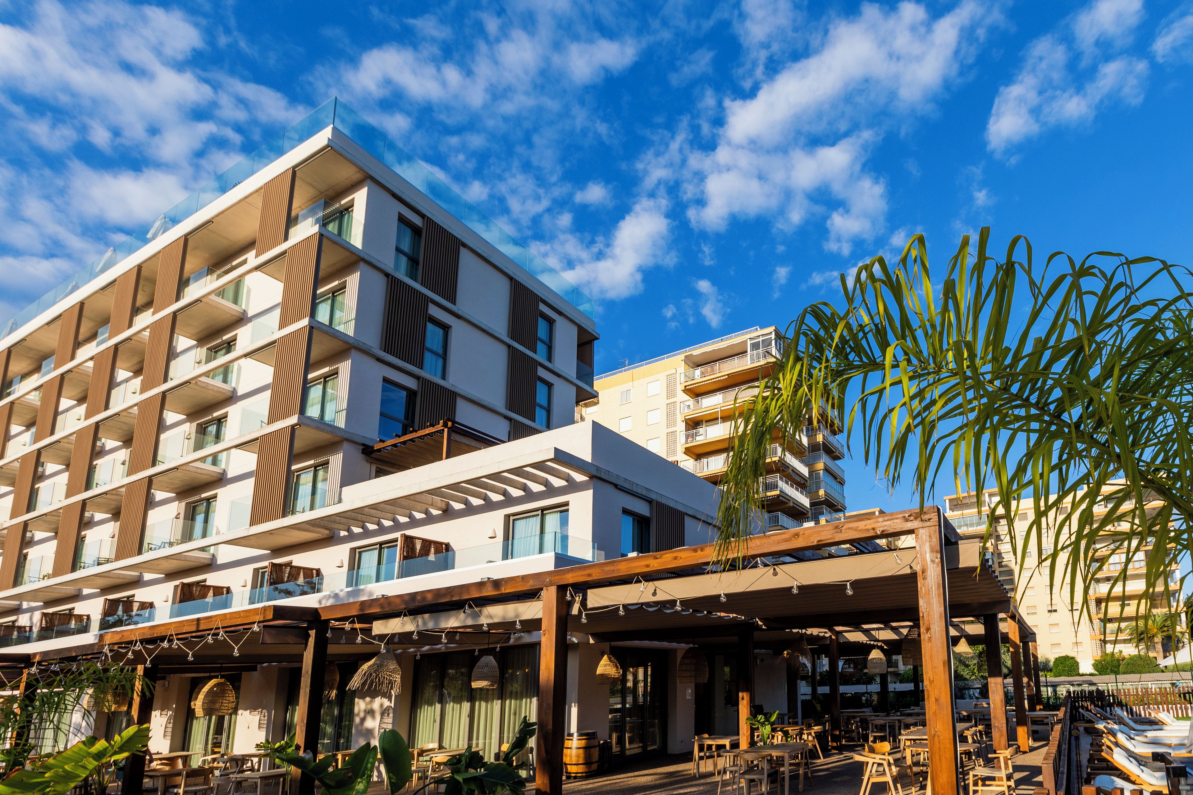 Un hotel de varios pisos con balcones, mobiliario exterior y una zona de piscina.