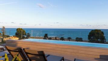 Zona junto a la piscina con sillones, vista al mar y cielo despejado.