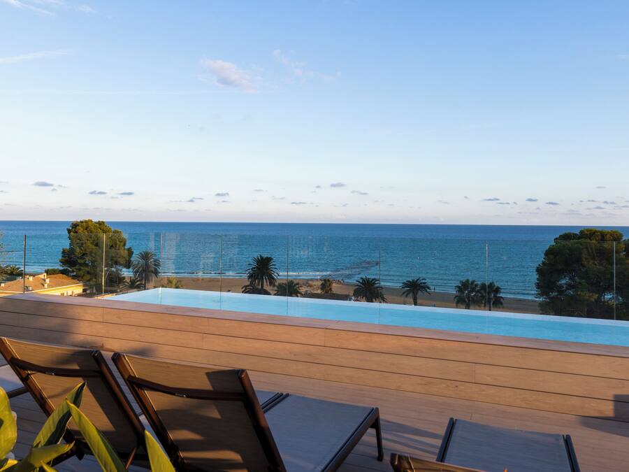 A poolside area with lounge chairs, a view of the sea, and a clear sky.