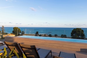 Zona junto a la piscina con sillones, vista al mar y cielo despejado.