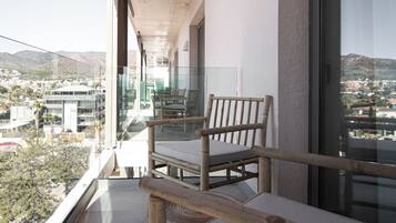 A balcony with a view of the city, a wooden chair, and a glass railing.
