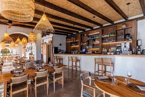 A restaurant with wooden tables and chairs, a bar area with shelves of bottles, and hanging wicker light fixtures. - Albades Hotel & Spa (Benicassim)