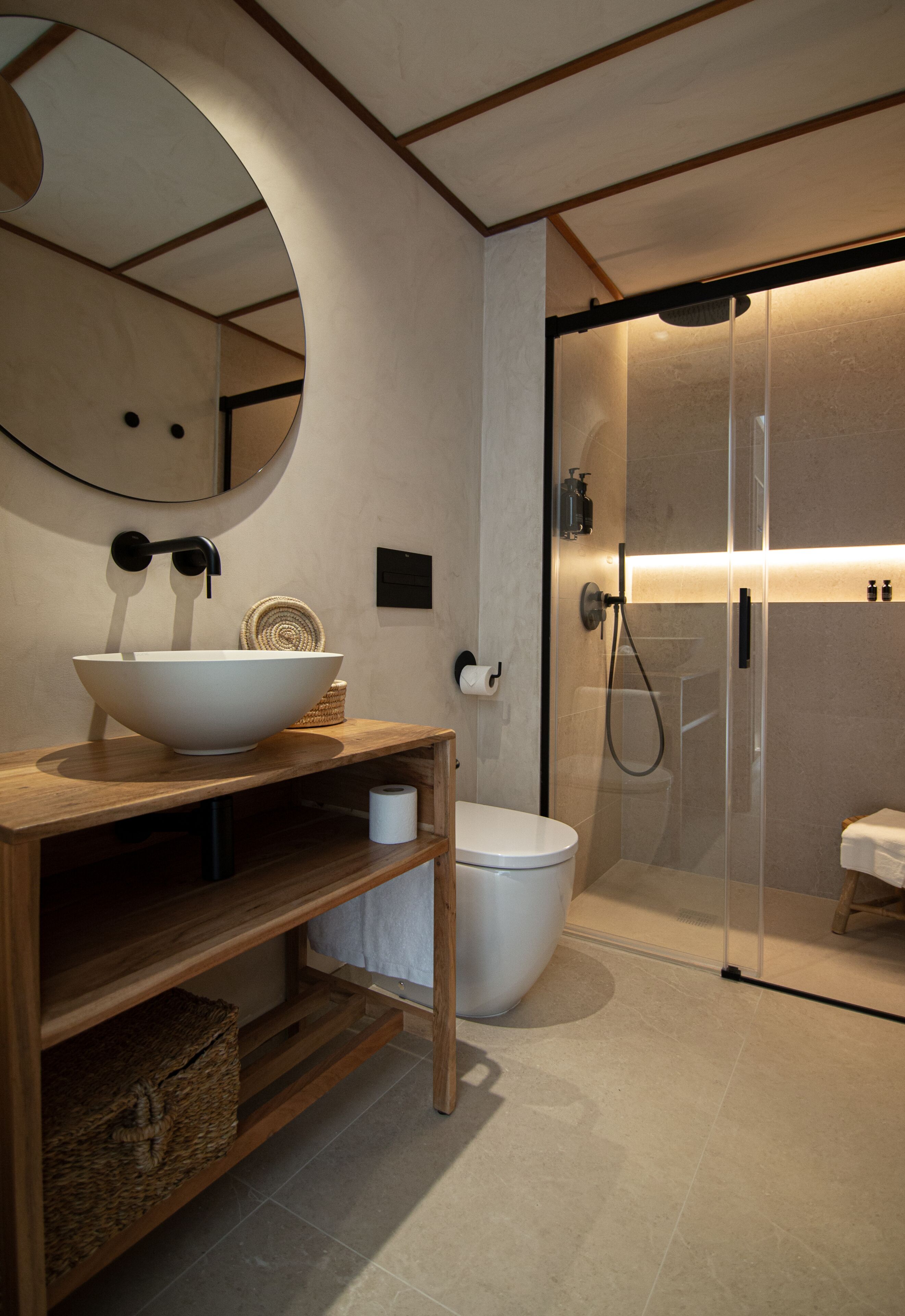 Bany modern amb un mirall oval gran, un tocador de fusta amb un lavabo, un vàter i una dutxa amb envàs de vidre.