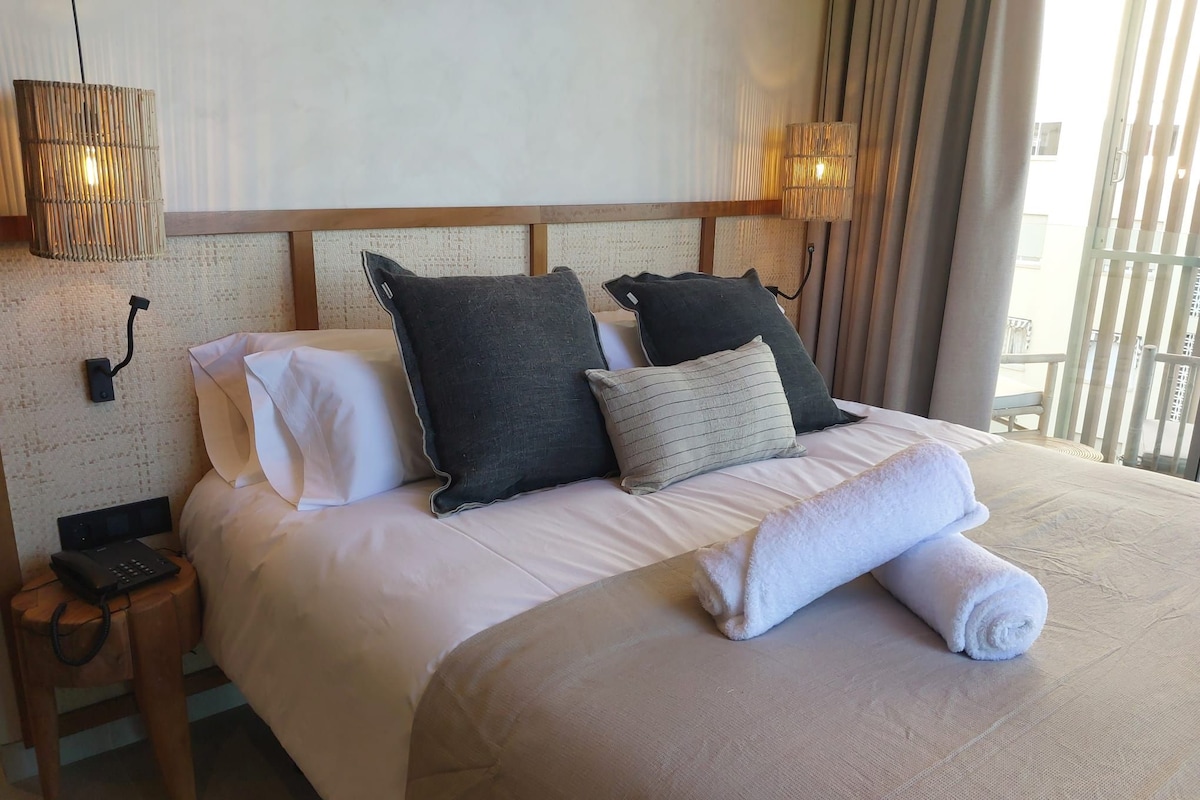 A neatly made bed with pillows, a bedside phone, and a lamp on a nightstand.