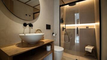 Un baño moderno con tocador de madera, un espejo grande, un lavabo blanco, un inodoro y zona de ducha con mampara de cristal.