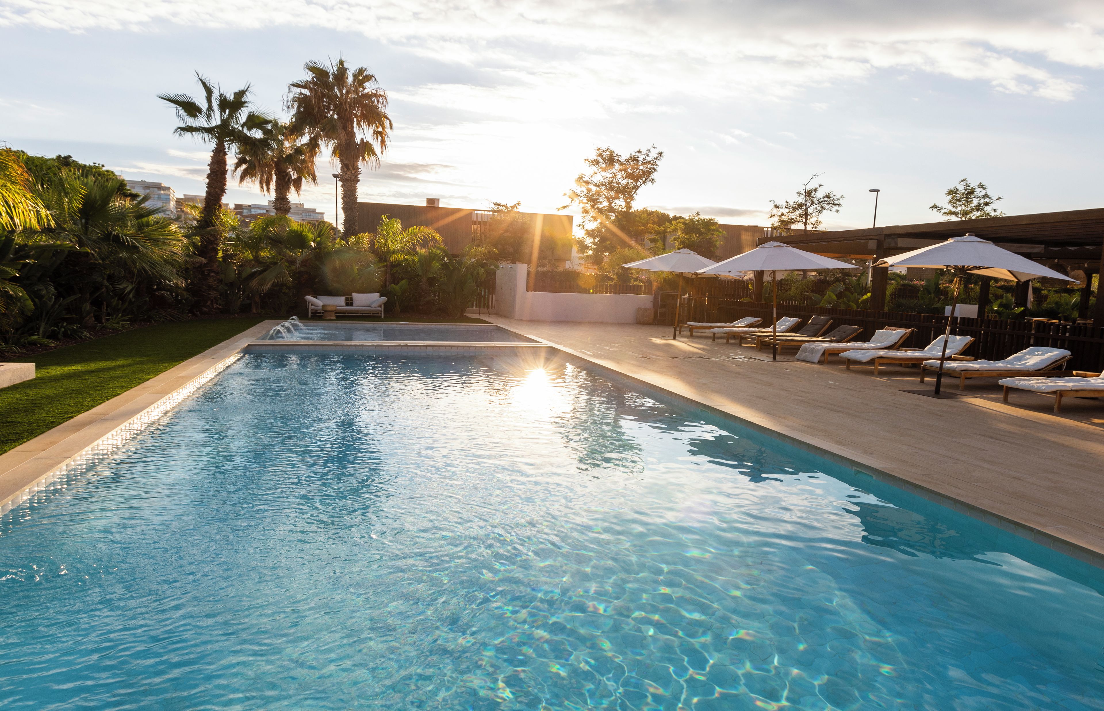 A swimming pool with lounge chairs and umbrellas, surrounded by palm trees and greenery.