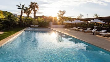 A swimming pool with lounge chairs and umbrellas, surrounded by palm trees and greenery.