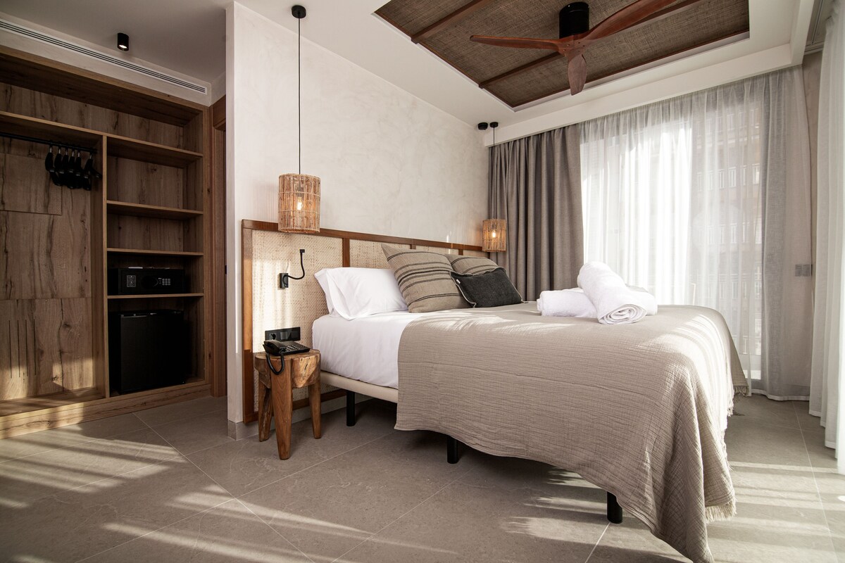 A bedroom with a bed, wooden wardrobe, and a small table.