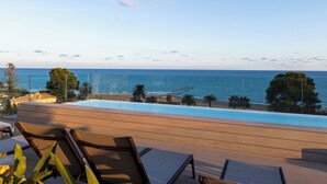 A poolside area with lounge chairs, a view of the sea, and a clear sky. - Albades Hotel & Spa (Benicassim)