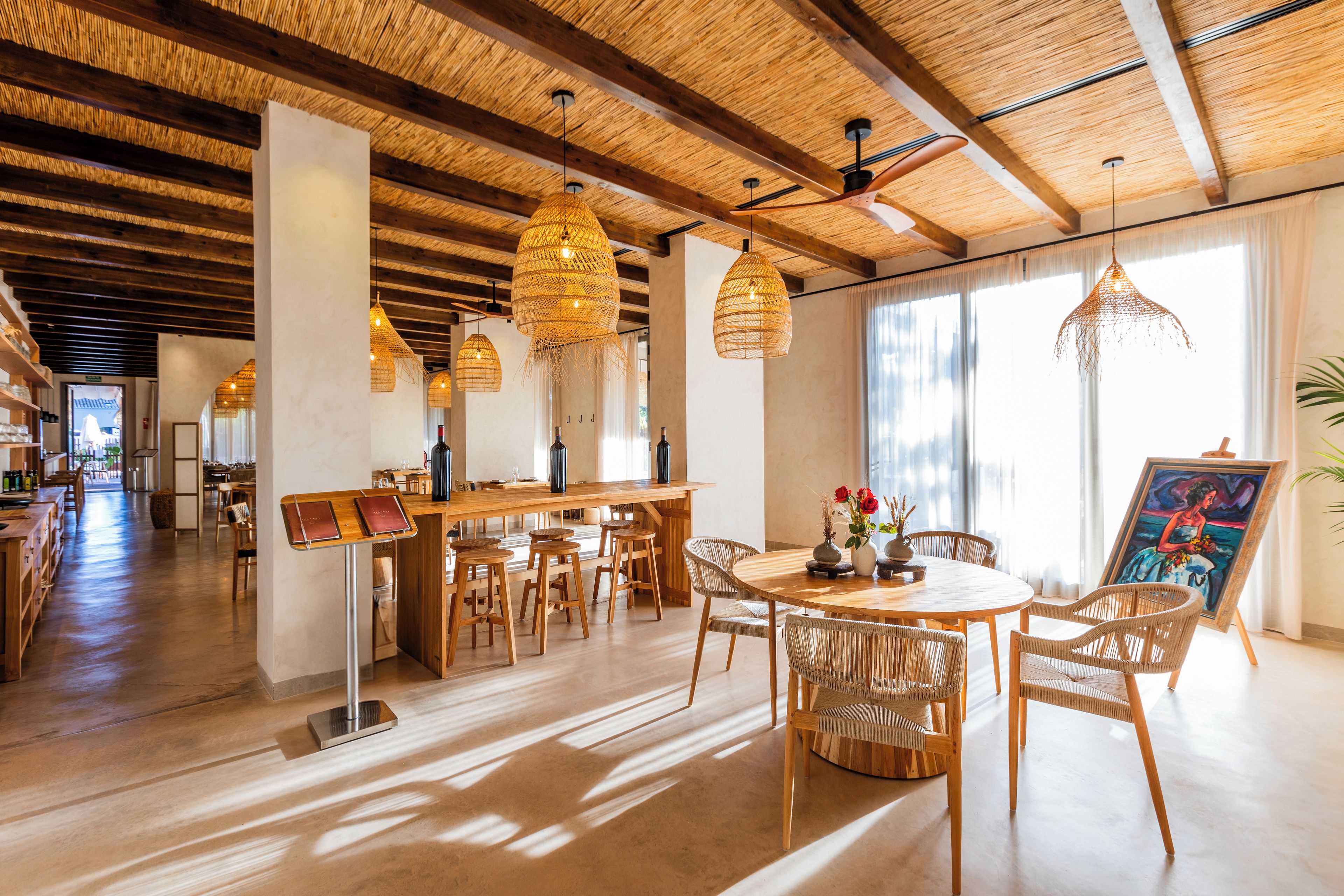 Un comedor amplio con una mesa de madera, sillas de mimbre y lámparas colgantes de mimbre.