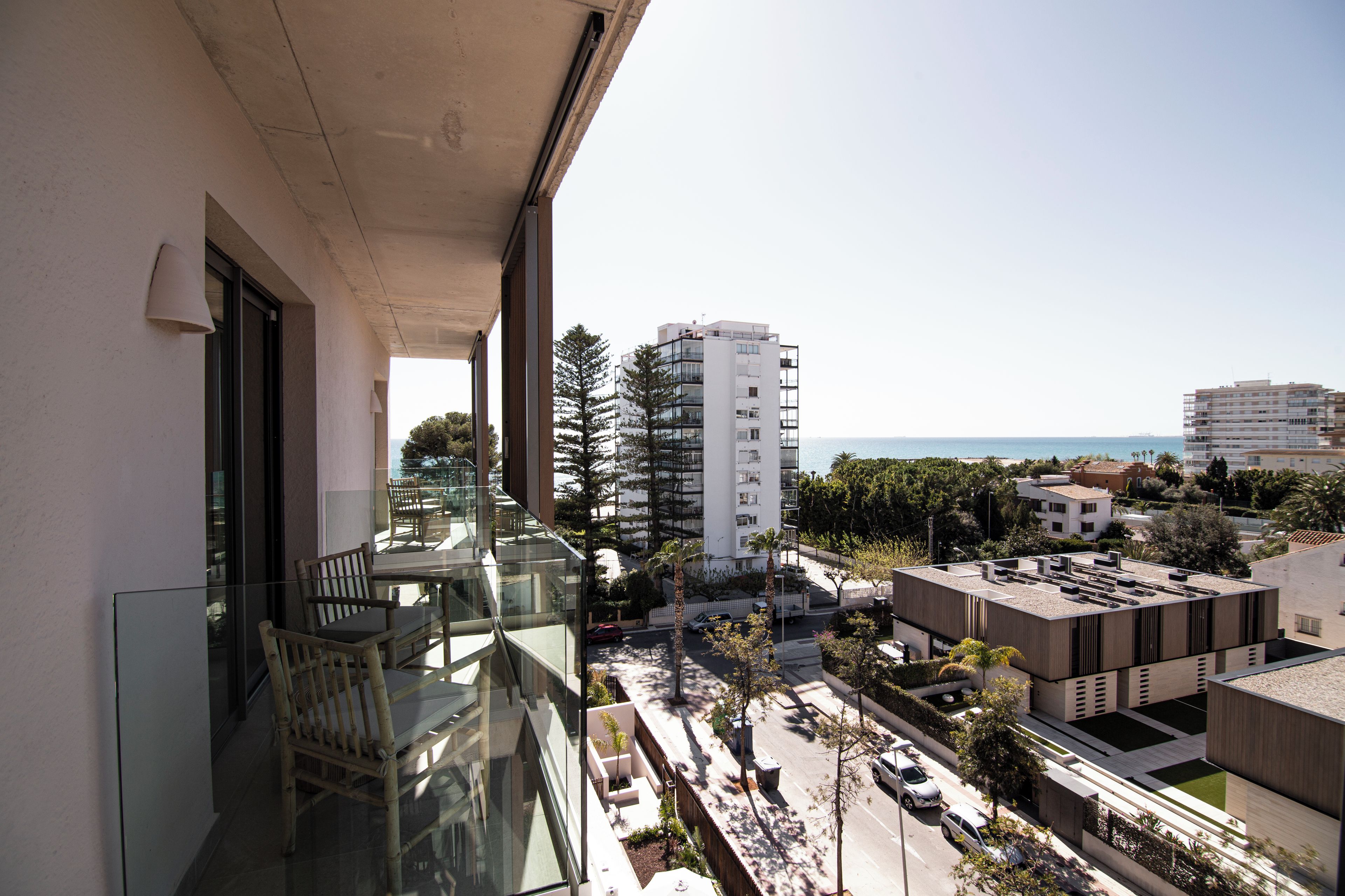 A balcony with glass railings, outdoor furniture, and a view of the cityscape and sea.