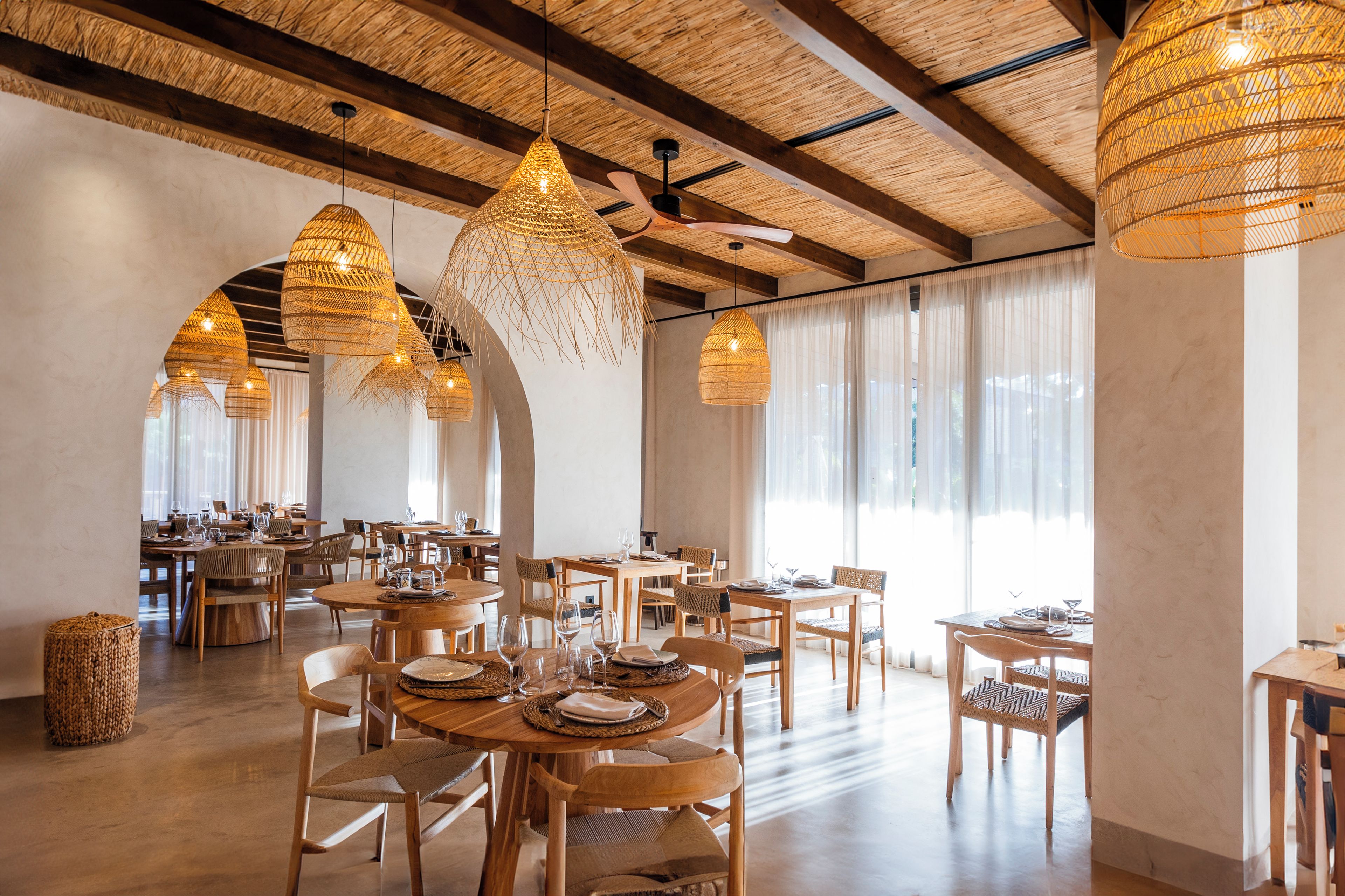 A spacious dining area with multiple tables and chairs, large woven pendant lights, and a ceiling fan.