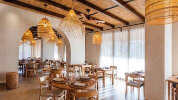 A spacious dining area with multiple tables and chairs, large woven pendant lights, and a ceiling fan.