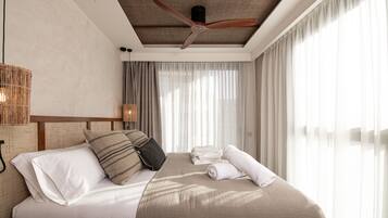Habitación de hotel con cama, ventilador de techo, ventana grande con cortinas y lámpara de techo de fibra.