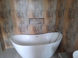Un bagno moderno con una vasca da bagno indipendente, un pannello a parete in legno e una piccola mensola rettangolare.