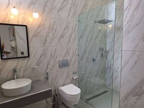 Un bagno con parete in marmo, un lavabo, un water e zona doccia con pareti in vetro.