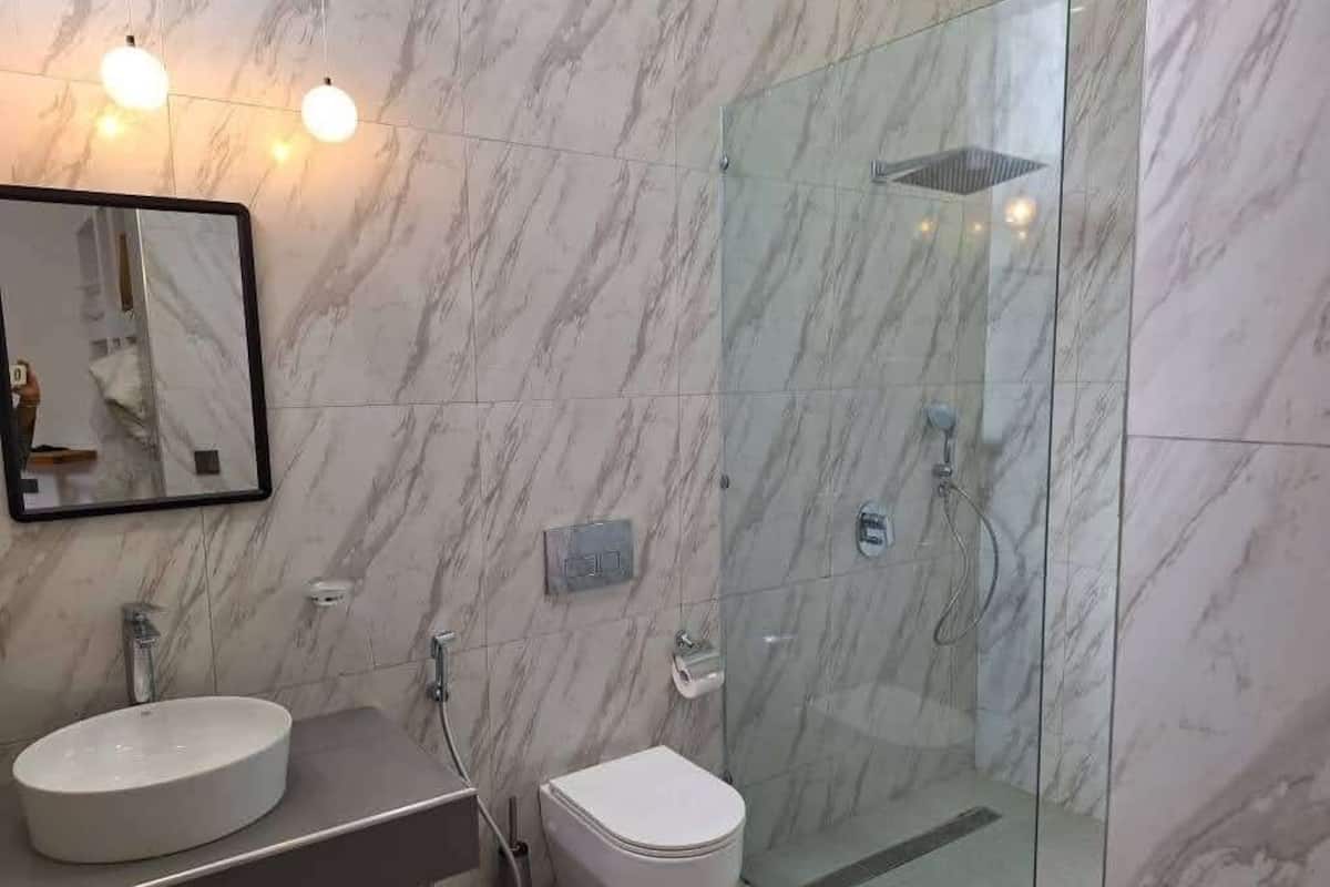 A bathroom with a marble wall, a sink, a toilet, and a glass-enclosed shower area.