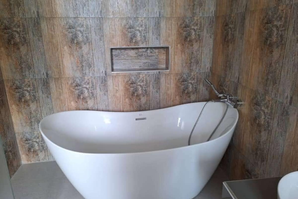 A modern bathroom with a freestanding bathtub, a wooden wall panel, and a small rectangular shelf.