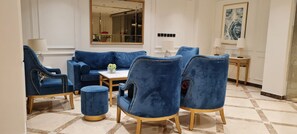 A room with a blue sofa set, a round ottoman, a small table with a vase, and a mirror on the wall. - Golden New Heraa (Jeddah)