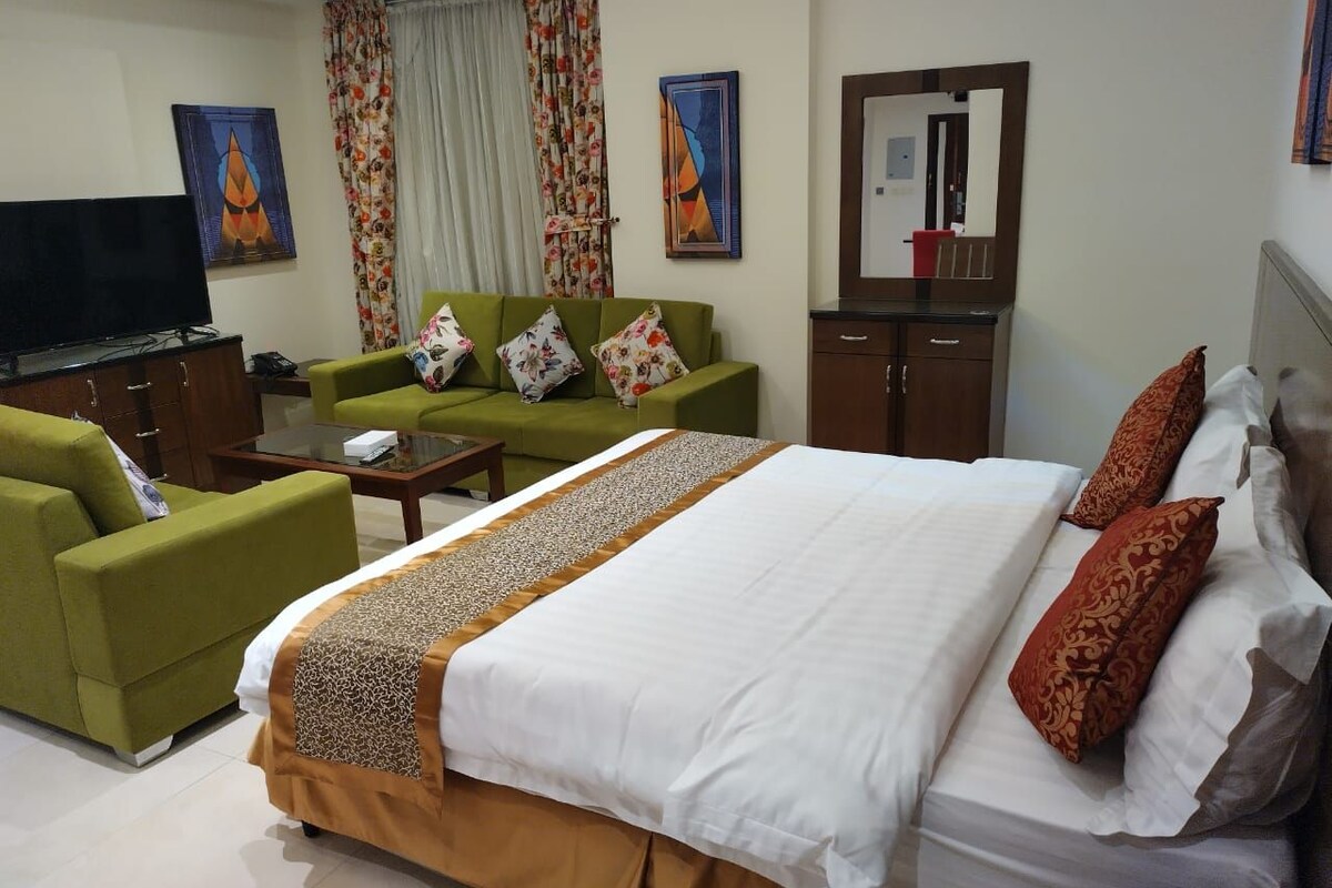 A hotel room with a large bed, a sofa, a television, and a desk.