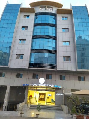 Un edificio moderno con facciata in vetro, un ingresso centrale con gradini e un cartello in arabo.