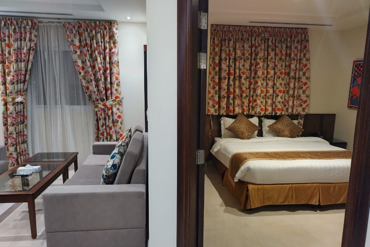 A hotel room with a bed, a sofa, a coffee table, and curtains.