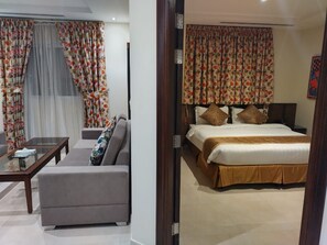 A hotel room with a bed, a sofa, a coffee table, and curtains. - Golden New Heraa (Jeddah)