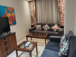 Een woonkamer met een bank, twee salontafels, een televisie op een kast en een schilderij aan de muur.
