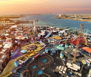 An aerial view of a coastal amusement park with various rides and attractions, including a Ferris wheel, roller coasters, and a large water slide. - Golden New Heraa (Jeddah)