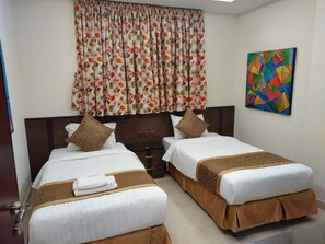 A hotel room with two beds, a wooden headboard, a floral curtain, and a colorful abstract painting on the wall. - Golden New Heraa (Jeddah)