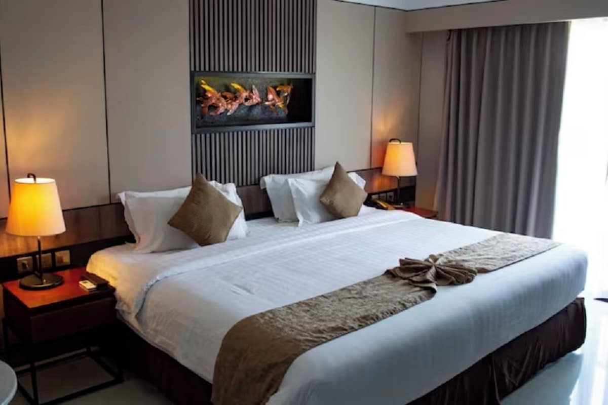 A hotel room with a large bed, two bedside tables with lamps, a flat-screen TV mounted on the wall, and a view of the outdoors through the window.