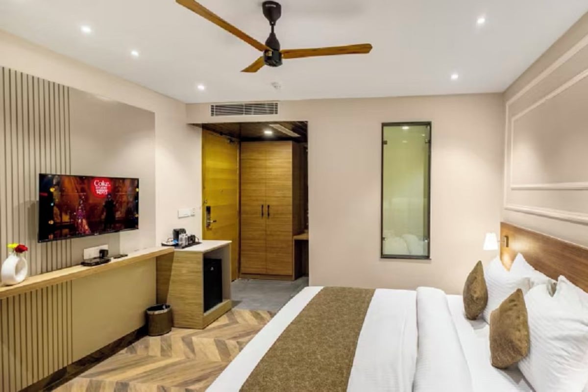 A hotel room with a bed, a TV, a desk, a wardrobe, and a ceiling fan.