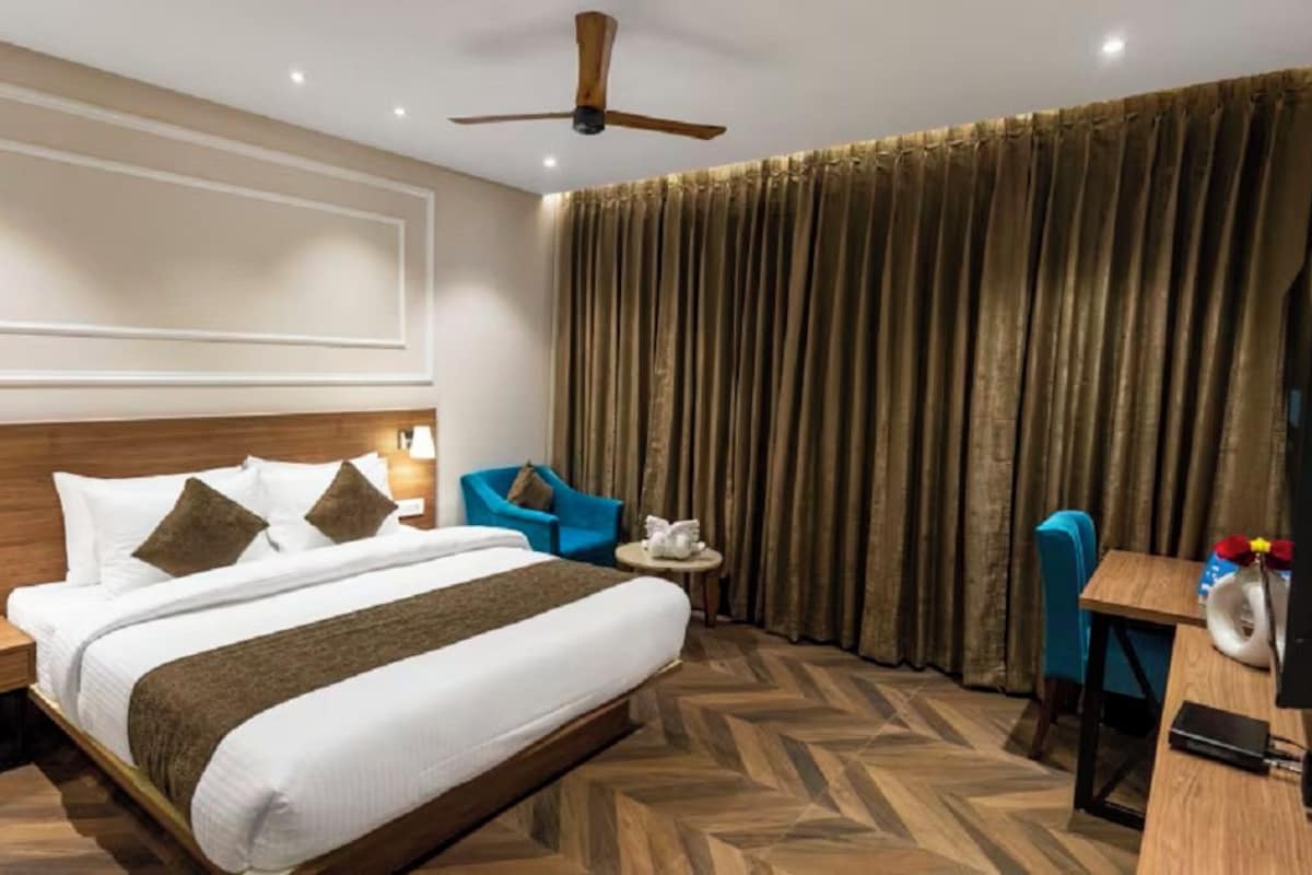 A hotel room with a bed, a desk, a chair, a ceiling fan, and a large window with curtains.