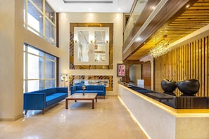 Um hall de entrada com balcão de recepção, assentos azuis, uma mesa de centro e um espelho grande.