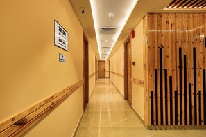A hotel hallway with directional signs, a fire alarm, and a wooden partition. - Pride Hotel Rishikesh (Narendranagar)