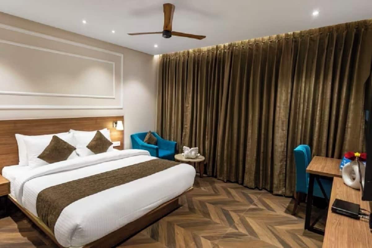 Ein Hotelzimmer mit Bett, Schreibtisch, Stuhl, Deckenventilator und einem großen Fenster mit Vorhängen.