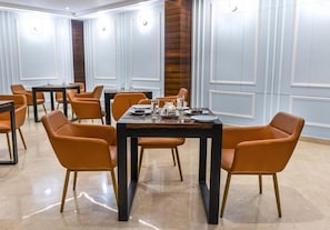 A conference room with a round table, orange chairs, and a wooden accent wall. - Pride Hotel Rishikesh (Narendranagar)