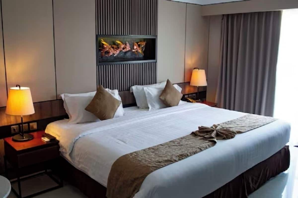 Ein Hotelzimmer mit einem großen Bett, zwei Nachttischen mit Lampen, einem an der Wand montierten Flachbildfernseher und Blick ins Freie durch das Fenster.