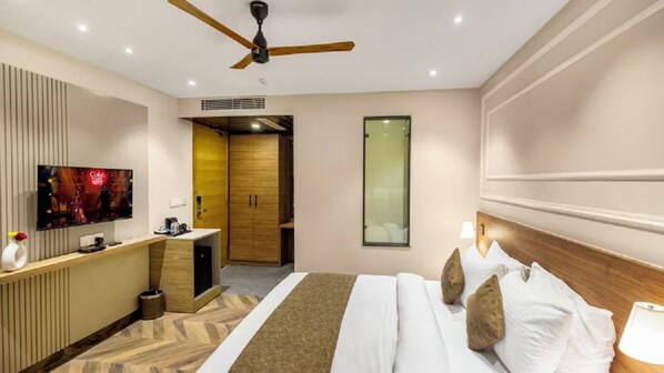 A hotel room with a bed, a TV, a desk, a wardrobe, and a ceiling fan. - Pride Hotel Rishikesh (Narendranagar)