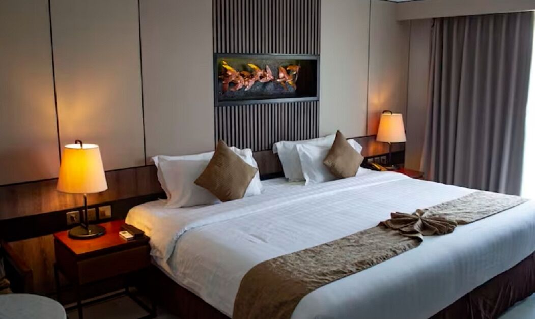 Habitación de hotel con una cama grande, dos lámparas de noche, un televisor de pantalla plana montado en la pared y una ventana con cortinas.