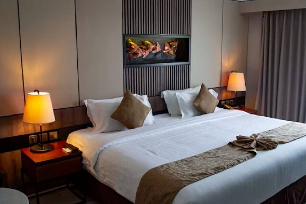 Habitación de hotel con una cama grande, dos lámparas de noche, un televisor de pantalla plana montado en la pared y una ventana con cortinas.