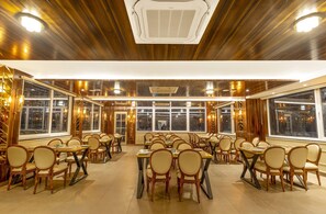 Um restaurante amplo com painéis de madeira, várias mesas e cadeiras.