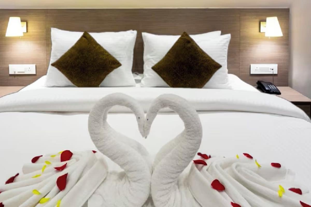 A hotel room with a bed, two nightstands, a phone, and a heart-shaped decoration on the bed.