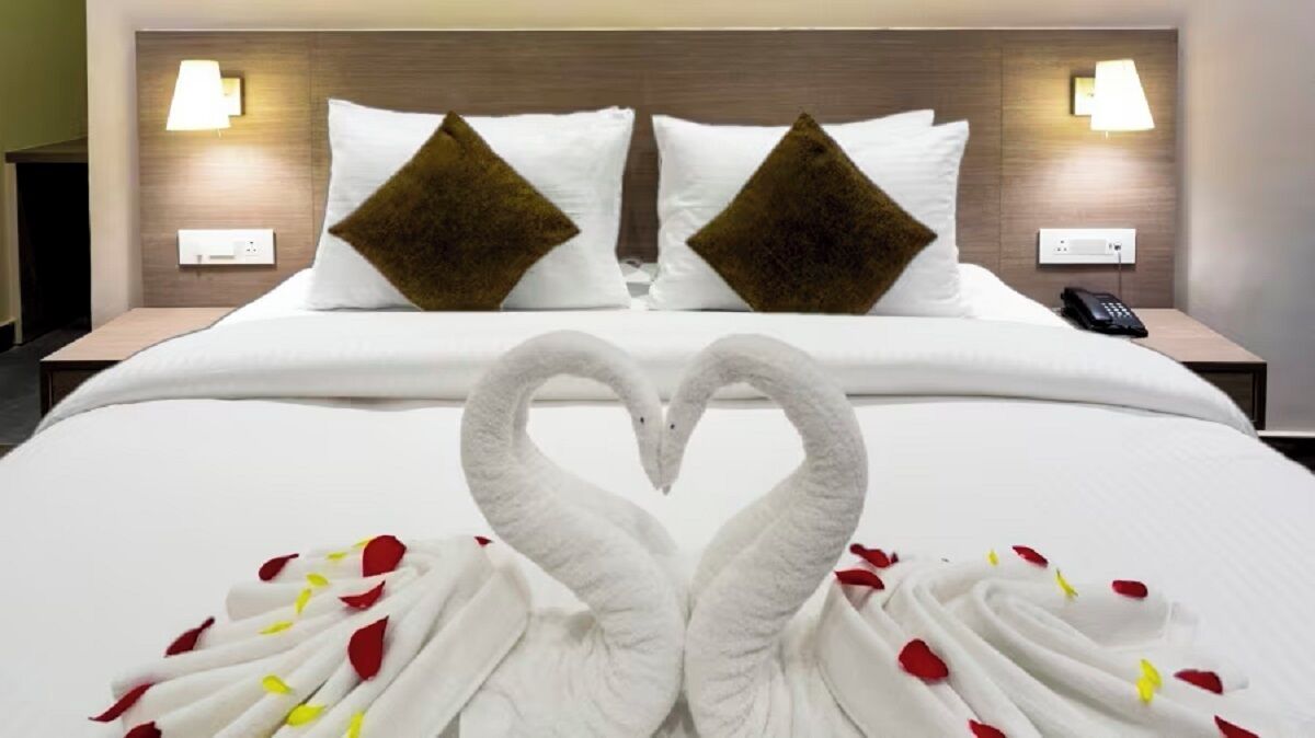 Habitación de hotel con cama, dos mesitas de noche, teléfono y una decoración con forma de corazón sobre la cama.