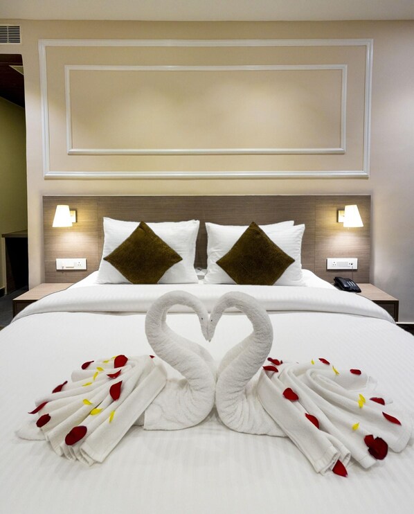 A hotel room with a neatly made bed, two pillows, bedside lamps, and a heart-shaped towel arrangement. - Pride Hotel Rishikesh (Narendranagar)