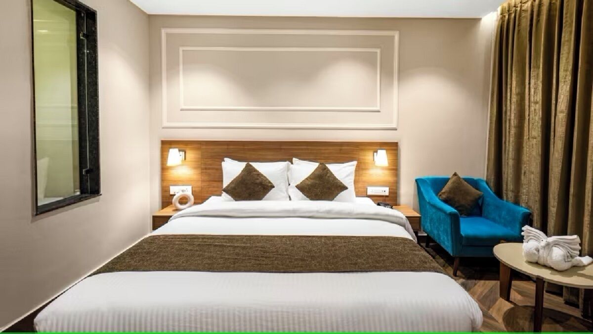 Habitación de hotel con una cama grande, dos lámparas de noche, un sillón azul y una mesita redonda con una toalla.