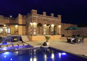 A swimming pool with lounge chairs and a stone building with arches.